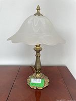 Full view of decorative table lamp showing frosted glass shade with scalloped edges and brass base with floral detailing.