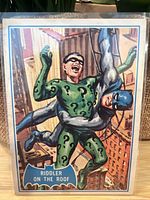 Front side of 1966 O-Pee-Chee Batman trading card number 37B showing Riddler in green costume with question marks and Batman in blue and grey grappling on a rooftop.