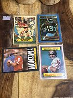 Four Joe Montana football cards laid out on wood surface including a rare Topps Dynasty and 1983 Record Breaker card