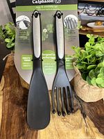 Front view of the Calphalon egg and omelette utensil set packaging showing two utensils: a spatula and a slotted turner, with stainless steel handles and black utensil heads.