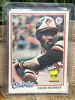 Front view of Eddie Murray rookie card showing player in Orioles uniform ready to bat, with 'Orioles' and 'Eddie Murray' text and Topps All-Star Rookie trophy symbol on bottom right.