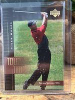 Tiger Woods Tour Time rookie card showing Woods mid-swing in red and black attire with gold text and Upper Deck logo.