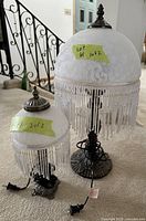 Photo showing two vintage lamps with metal bases, frosted white glass shades, and hanging white bead fringe. Electrical cords visible at bases.