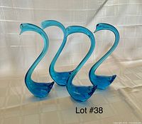 Four vintage blue glass swan figurines displayed on a white textured cloth background, clearly showing the shape and blue color of each swan.