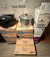 View of multiple cardboard boxes stacked with two pots on top: a black speckled enamelware pot with lid and ladle, and an aluminum pot with lid. Boxes labeled for medical supplies and food container brand Zenith.