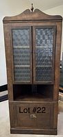 Front view of an antique wooden corner cabinet showing two glass doors with circular patterned glass, three interior shelves, an open bottom corner shelf, and a storage drawer with brass handle below.