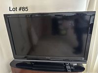 Sony Bravia flat screen TV, remote control, and black stand base shown from the front, screen off.