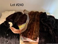 Three long fur coats in various shades with multiple fur collars and accessories arranged on a bed.