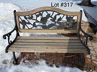 Front view of the garden bench in an outdoor setting with snow on the ground. Shows wood slat seat and floral metal backrest with armrests and legs.
