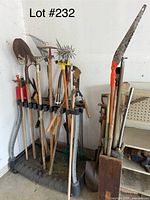 Photo of assorted garden tools including shovels, rakes, hoes, pitchfork, a pruning saw with an orange handle, hedge trimmers with yellow and black parts, all inserted into two different garden tool stands.