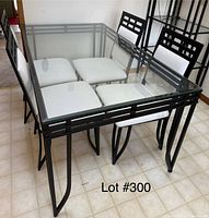 Glass top rectangular kitchen table with 4 black metal frame chairs with white cushions arranged around it.