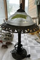 Photo of metal table lamp featuring frosted glass floral shade, detailed metal rim, and dark metal base with electrical cord.