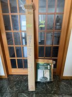 Two boxed items, a long box containing the patio umbrella and a smaller boxed cast iron umbrella base, shown side by side indoors against glass panel doors.