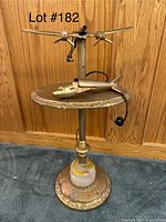Full view of vintage airplane-themed end table lamp with metal airplane decoration, round tabletop, and ornate metal base showing wear and tear.