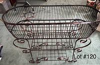 Metal planter with oval shape, vertical bars, scroll legs, and a lower shelf for additional storage or decoration.