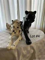 Both figurines on a white checkered cloth table in front of closed curtains, Dalmatian on left and jaguar on right