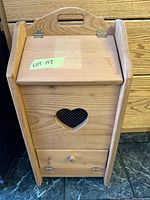 Photo of wooden potato/onion storage bin showing front with heart-shaped ventilation cutout, flip-top lid, and bottom drawer.