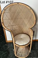 Vintage medium-sized rattan peacock chair with woven rattan body and round beige seat cushion against a wall.