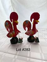 Photo of two vintage hand-painted red rooster wood carvings with floral patterns taken on a white cloth background.