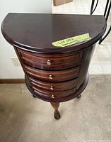 Half-moon dark wood side table with four drawers and three cabriole legs.