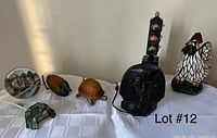 Overview of six figural table lamps on white tablecloth: green stained glass turtle, two amber glass shell turtles, black pharaoh bust, vertical traffic light, stained glass rooster.