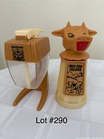 Photo shows two vintage kitchenware items: Moo-Cow Creamer with cow head lid, and square sugar dispenser with beige lid and sugar label.
