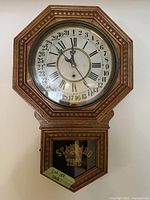 Photo of the vintage William Gilbert octagonal wooden wall clock showing the clock face with Roman numerals and 24-hour numbers around the edge, and the lower glass compartment with 'STANDARD TIME' lettering and part of mechanism visible.