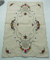 Full view of the cream linen table runner showing floral cross stitch embroidery and crocheted inserts along scalloped edges.