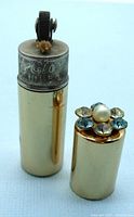 Full view showing the brass-tone lighter with cap removed revealing ignition wheel and wick, and the cap decorated with rhinestones and faux pearl on top.