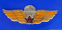 Front view of miniature Canadian Army parachute jump wings insignia with orange enamel wings, silver parachute, and red maple leaf star center
