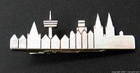 Front view of silver-tone tie bar with Cologne skyline silhouette on a black background showing the detailed skyline shape and polished finish.