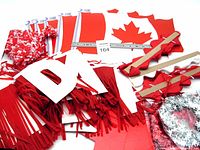 Top-down view showing packaged and unwrapped red and white crepe paper fringe banners, Canadian flag cutouts, and other decorations spread out on a white surface