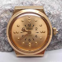 Front view of Arsa braille watch showing gold-tone case and dial with embossed braille dots for tactile reading of time.