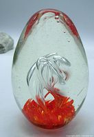 Full front angle of the clear glass egg paperweight featuring internal orange swirl and flame design with bubbles inside the glass