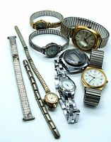 Top view of assortment of nine vintage wristwatches and watch bands on white surface showing various sizes and styles of metal bands and watch faces.