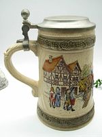 Left side view showing detailed ceramic relief scene of village and people awaiting beer wagon, with pewter lid closed.