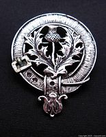 Front view of the silver-tone brooch with detailed thistle clan crest badge design and buckle accent.