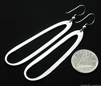 Pair of long open oval-shaped sterling silver earrings with hook wires, shown next to a coin for scale.