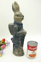 Side and front angled view of 14 inch tall salt glaze Easter rabbit figurine with clothing and basket detail, shown next to standard Campbell's soup can for size reference.