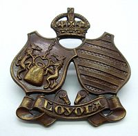 Front view of bronze Canadian Officers' Training Corps cap badge with dual shields, crown and 'Loyola' banner.