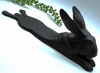 Side angle view of black cast iron bunny rabbit door stop showing profile with ears upright and extended body.