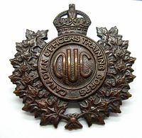 Oblique front view of the bronze Canadian Officers' Training Corps Queens University cap badge showing detailed maple leaves with crown and "QUC" inscription