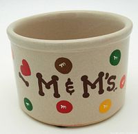 Front view showing M&M's lettering in brown with colored candy spots on cream pottery crock.