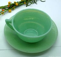 Side angle showing translucent pale green jadeite glass cup with handle and matching saucer with ribbed edge.