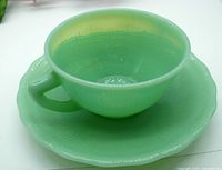 Translucent green jadeite glass cup placed on matching saucer, showing rounded cup shape and ribbed interior texture.