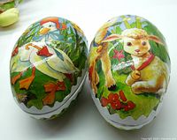 Two vintage German paper mache Easter eggs shown side by side with colorful painted images of a duck and a lamb with a goat on the exterior.