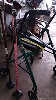 Green walker with seat and brakes, leaning with two canes and miscellaneous accessories