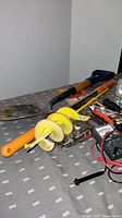 Yellow-handled small shovel, two yellow auger drill bits, hammer, and other tools on table.