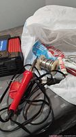 Photo showing small red soldering tool with attached power cord and plug alongside solder spool and rosin core solder tube on a surface