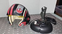 View of the Poe Dameron helmet and flight simulator joystick side by side on a table with gray patterned cloth.